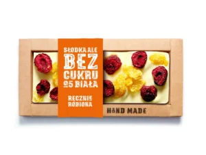 Ręcznie robiona biała czekolada bez cukru z owocami, zapakowana w ekologiczne pudełko z napisem na pomarańczowym tle.