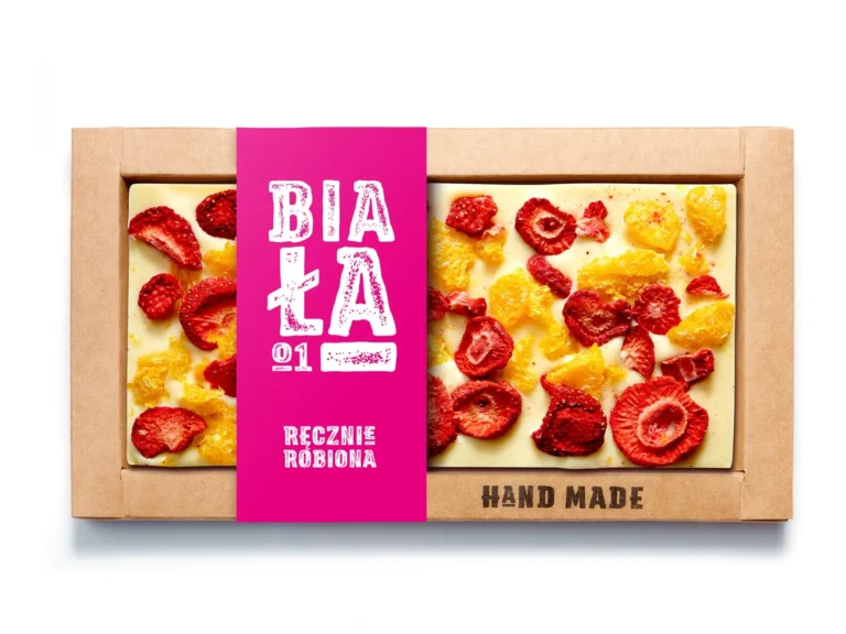 Ręcznie robiona biała czekolada z suszonymi truskawkami i cytrusami w kartonowym opakowaniu z różowym akcentem.