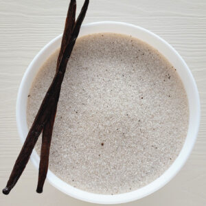 Biała miska z wanilinowym cukrem, ozdobiona dwoma strąkami wanilii na jasnym tle.