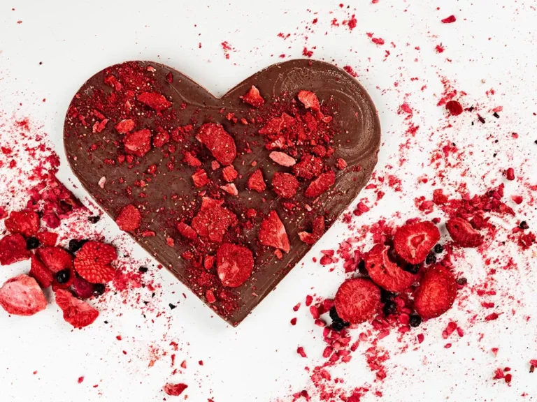 Czekoladowe serce z kawałkami liofilizowanych truskawek i malin na białym tle.