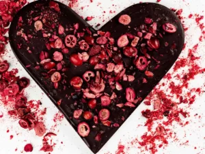 Serce z gorzkiej czekolady z suszonymi owocami na białym tle, ozdobione malinami i wiśniami.