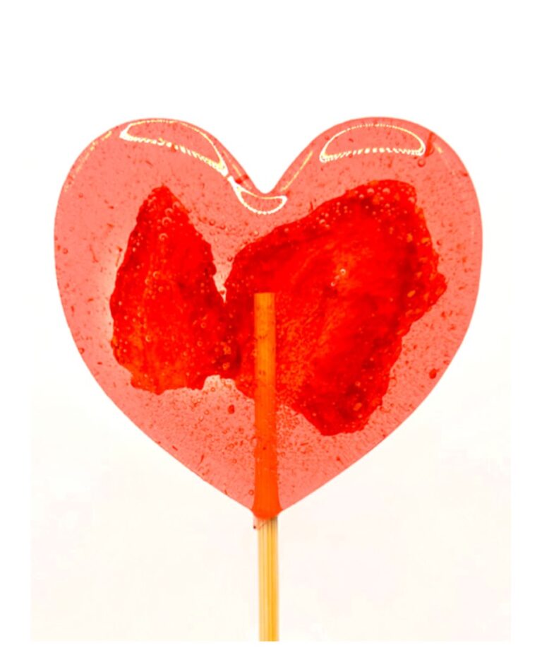 Czerwone lizakowe serce na patyku, zrośnięte wokół suszonej truskawki, na białym tle.